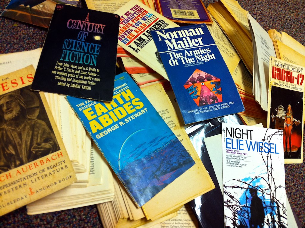 A pile of guillotined paperbacks with their covers and loose text blocks, including Auerbach's Mimesis, Delany's Babel-17, Elie Wiesel's Night, and Mailer's The Armies of the Night.